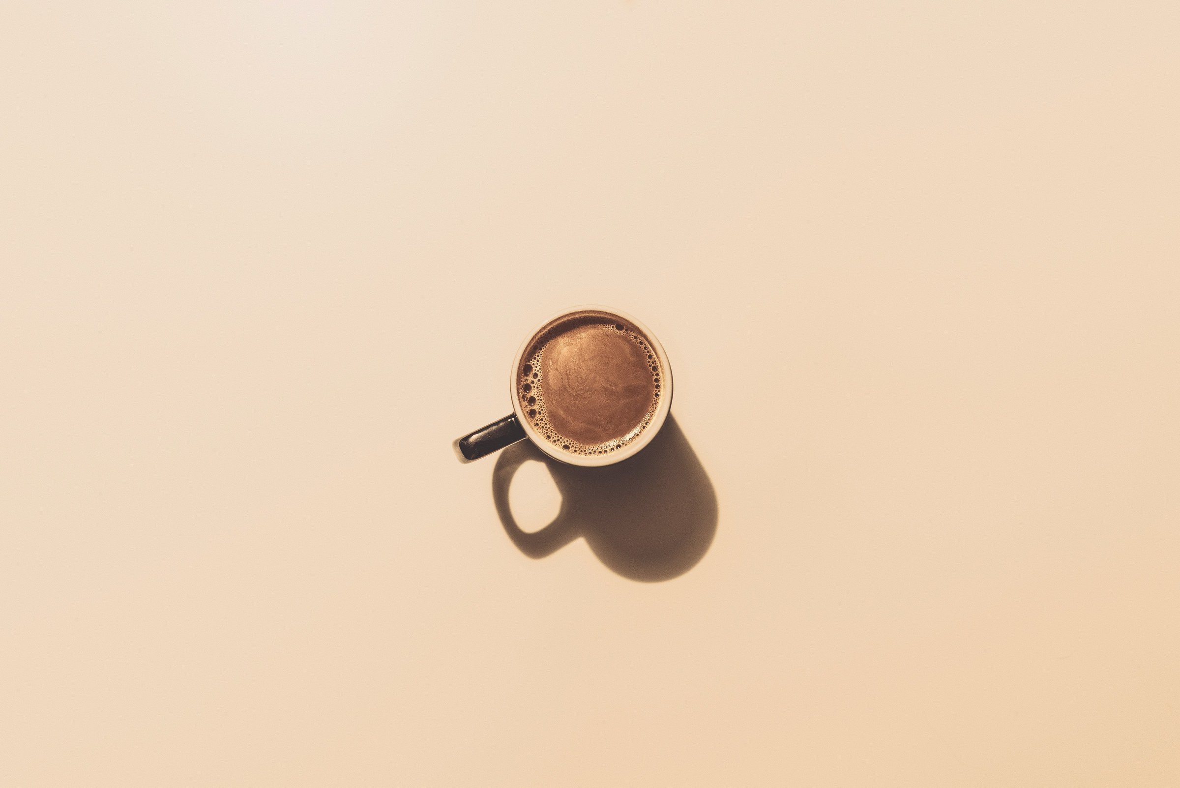 Eén koffiekopje met een lange schaduw, verder niets, op een verlaten vlak oppervlak.