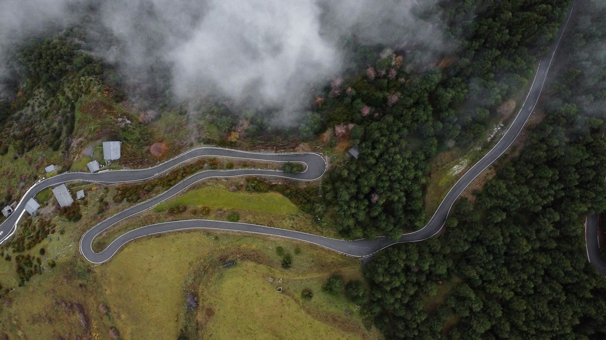 Bergpas van boven: haarspeldbochten door bos en mist.